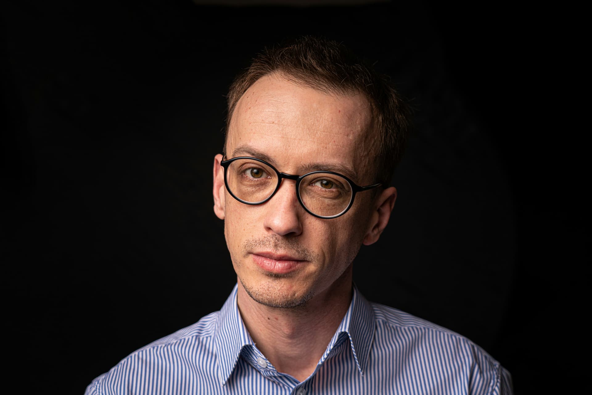 Man in a blue striped shirt against a black background.