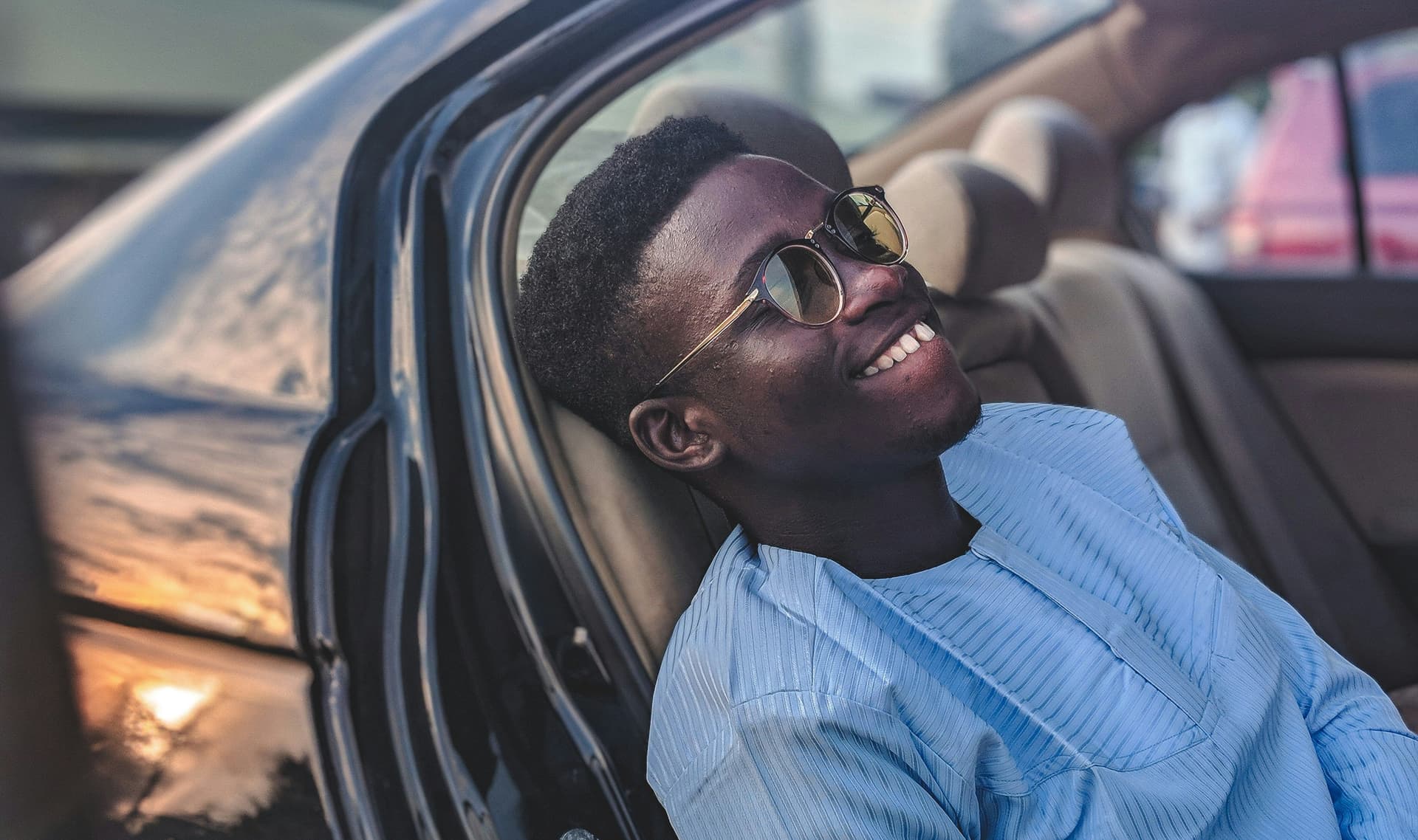 Person in a blue shirt in a car with the interior and sunset reflections visible.